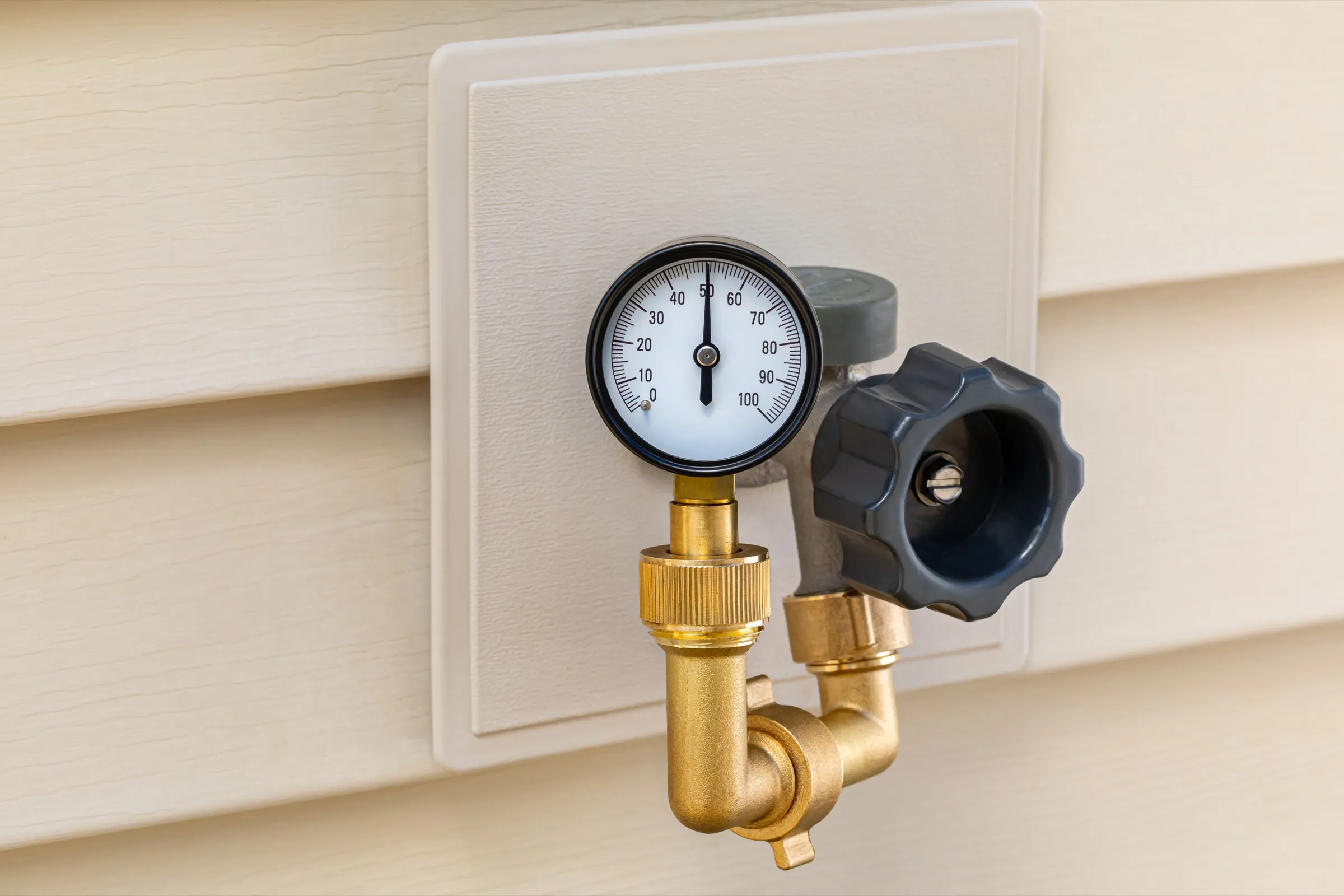 Brass test gauge threaded onto an outdoor faucet against home siding, used to verify a plumbing system holds after repairs.