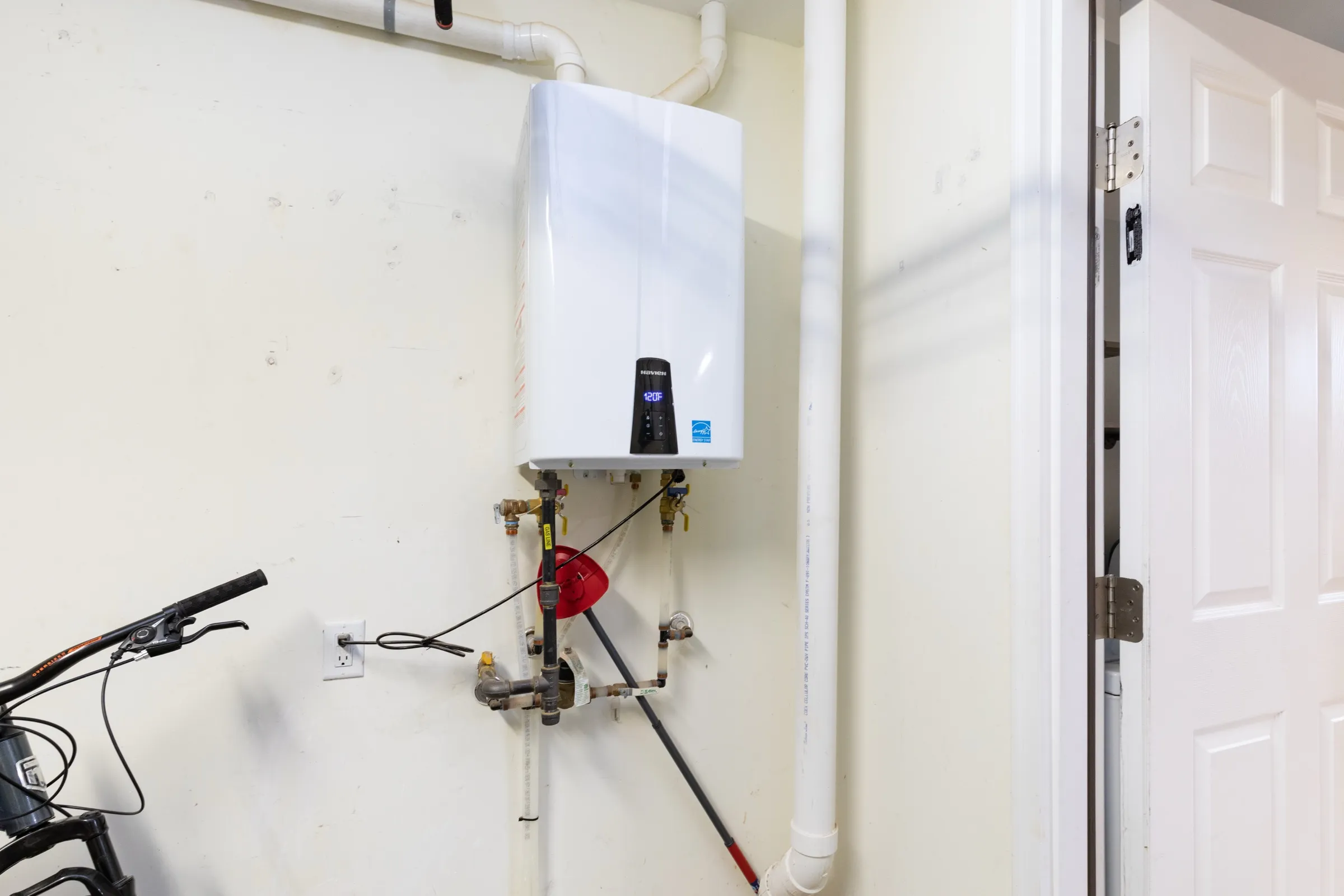 Wall-mounted tankless water heater installed in a garage, with water and gas connections plumbed neatly below the unit.