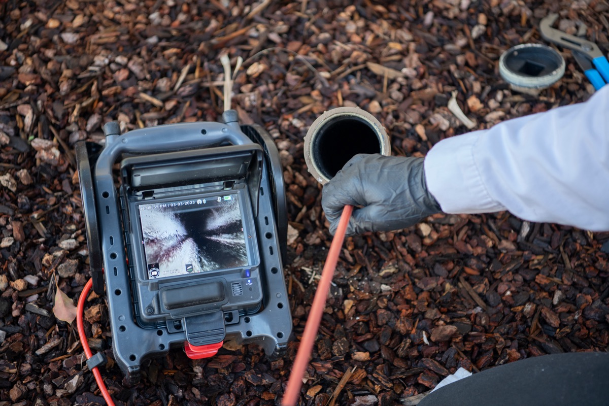 Technician running a pipe inspection camera into a sewer cleanout, watching the line on the monitor